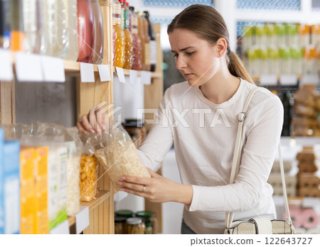 Girl customer in supermarket choose and take flakes from shelve, buy food stuff in grocery store Girl customer in supermarket choose and take flakes from shelve, buy food stuff in grocery store 122643727