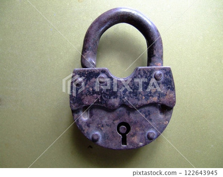 A vintage padlock showcases its weathered metal surface and distinctive shape as it rests flat on a green background. The keyhole is positioned at the center, inviting curiosity about its history. A vintage padlock showcases its weathered metal surface and distinctive shape as it rests flat on a green background. The keyhole is positioned at the center, inviting curiosity about its history. 122643945