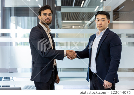 Two professional businessmen shaking hands in modern office setting symbolizing business agreement, partnership, teamwork. Depicts concepts of professionalism, collaboration, success in corporate 122644075