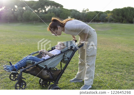 Mother talking with her son sitting in a stroller in a park Mother talking with her son sitting in a stroller in a park 122645298