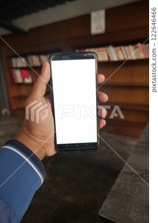 A Person Holding a Smartphone with a Blank Screen Inside a Library Setting 122646466