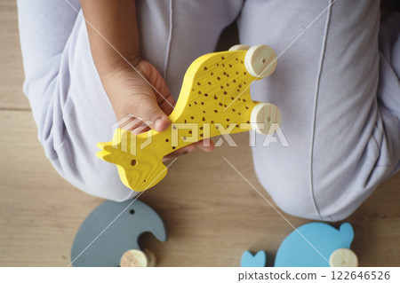 Child playing with colorful wooden animal toys on a wooden floor during a sunny afternoon Child playing with colorful wooden animal toys on a wooden floor during a sunny afternoon 122646526