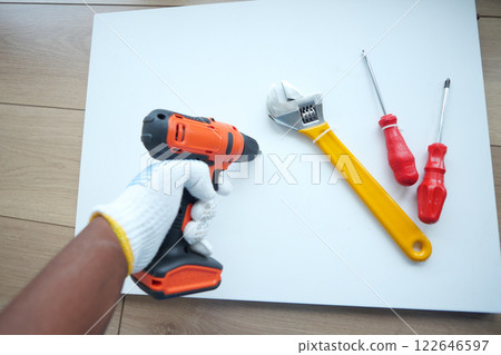Hand holding power drill and tools on flat surface for DIY project Hand holding power drill and tools on flat surface for DIY project 122646597