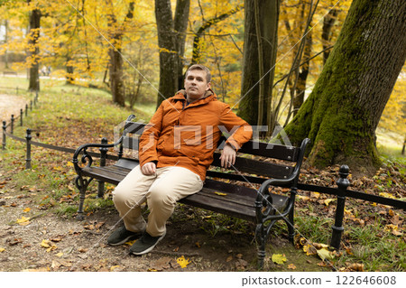 Young sad 30s man sitting alone on bench in autumn park. Thinking about life. Spending time alone in nature. Tired lost human guy wait, worship God 122646608