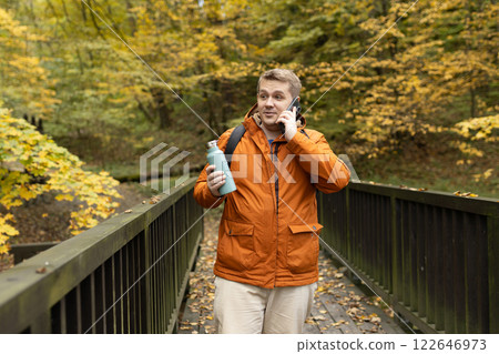 Technology mobile cellphone. Young Caucasian male talking on the smartphone at the park. Autumn season Road trip, food, travel, technology and people concept. High quality photo 122646973