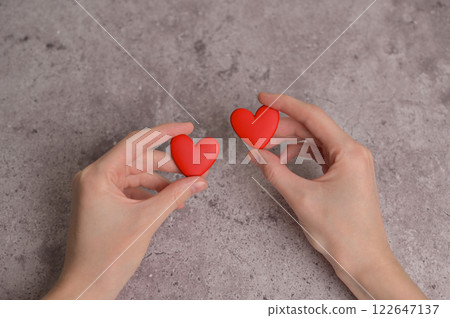 Woman holding couple of red earrings heart shape in hands. Gray concrete background. Blood donor donation Woman holding couple of red earrings heart shape in hands. Gray concrete background. Blood donor donation 122647137