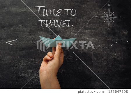 A hand holding a paper boat on a chalkboard with the words Time to Travel A hand holding a paper boat on a chalkboard with the words Time to Travel 122647308