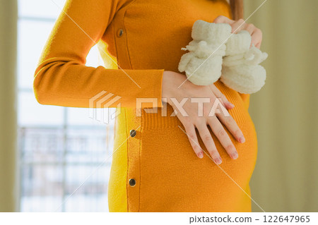 Pregnancy motherhood people expectation future. Big belly of pregnant woman, newborn baby booties in hands close up. Mom enjoying pregnancy relaxing at home. Maternity tenderness parenthood new life 122647965