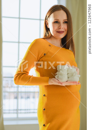 Pregnancy motherhood people expectation future. Pregnant woman with big belly holding newborn baby booties smiling at home. Young mom enjoying pregnancy. Maternity tenderness parenthood new life 122647968