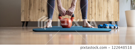 Fit woman holding an 8 kilogram kettlebell weight between her legs 122648518
