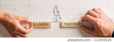Hands of a businessman and businesswoman holding two wooden pegs with a Stronger together sign Hands of a businessman and businesswoman holding two wooden pegs with a Stronger together sign 122648520