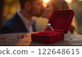 A diamond engagement ring in a red box is prominently displayed as a couple kisses softly in the background. Concept of true love. 122648615