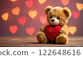 A cute plush toy bear holding a red heart against a backdrop of blurred, glowing hearts. Concept of tenderness. 122648616