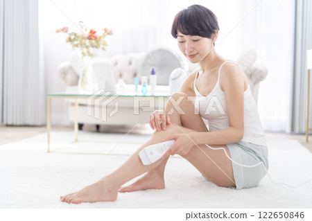 A middle-aged woman applying light hair removal to her legs A middle-aged woman applying light hair removal to her legs 122650846