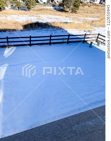 A serene backyard is blanketed in a fresh layer of snow on a bright sunny morning A wooden fence separates the yard from an open field with dried grass and scattered trees Shadows cast by the fence A serene backyard is blanketed in a fresh layer of snow on a bright sunny morning A wooden fence separates the yard from an open field with dried grass and scattered trees Shadows cast by the fence 122650945