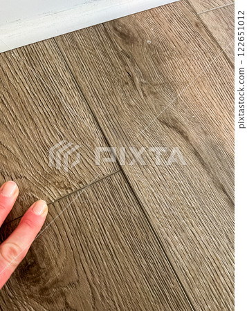 A close up view of vinyl plank flooring with visible gaps between the planks A hand is shown touching the surface highlighting the misalignment The wood grain texture of the planks gives a natural A close up view of vinyl plank flooring with visible gaps between the planks A hand is shown touching the surface highlighting the misalignment The wood grain texture of the planks gives a natural 122651012