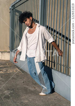 A handsome young Latino man holding onto a large fence at the entrance of a building with a friendly, happy expression 122651819