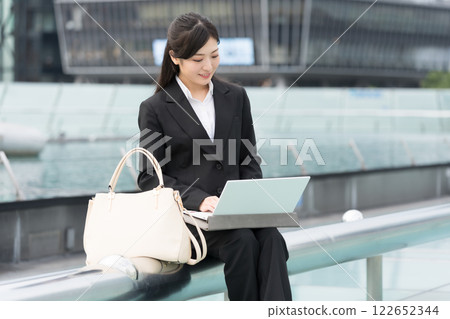 A smiling businesswoman looking at a laptop outdoors at the Water Spaceship, OASIS21, Sakae, Nagoya A smiling businesswoman looking at a laptop outdoors at the Water Spaceship, OASIS21, Sakae, Nagoya 122652344
