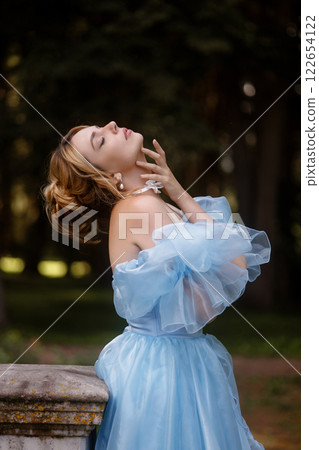 Romantic Woman in a Light Blue Gown Posing on a stone balustrade in a picturesque garden. Romantic Woman in a Light Blue Gown Posing on a stone balustrade in a picturesque garden. 122654122