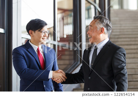 Asian businesspeople having a discussion together while walking inside the office building. Manager is talking with senior manager or chief of management. Businessmen in action portrait. 122654154
