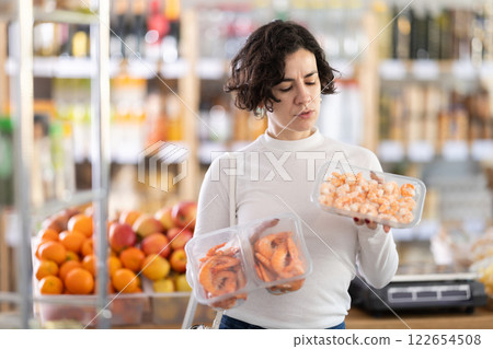 Adult woman chooses prawns in grocery store Adult woman chooses prawns in grocery store 122654508