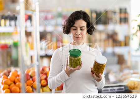 In store, woman near counter are looking at pickled green olives jar 122654529