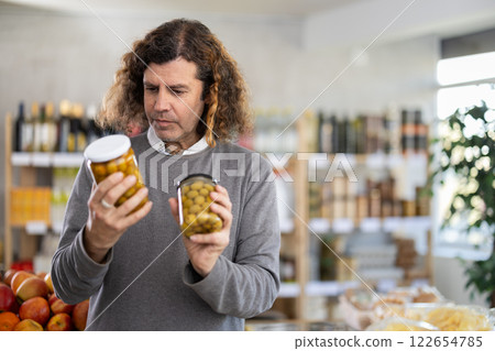 Male shopper choosing canned green olives in supermarket Male shopper choosing canned green olives in supermarket 122654785