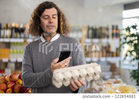 Male buyer scans QR code on packaging of chicken eggs label in grocery store 122654881
