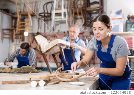 Professional craftswoman restorer in uniform renewing old-fashioned chair while working in repair shop Professional craftswoman restorer in uniform renewing old-fashioned chair while working in repair shop 122654938