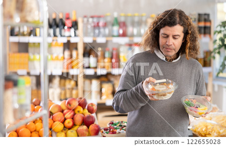 Choose food in supermarket - man chooses poke to buy in the grocery department section of store 122655028