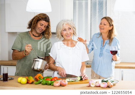 Cheerful couple and old woman drinking wine and cooking in the kitchen at home Cheerful couple and old woman drinking wine and cooking in the kitchen at home 122655054