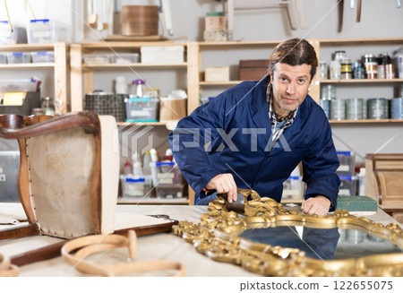 Portrait of middle-aged skillful repairman carpenter renovating mirror frame using tools in woodwork studio Portrait of middle-aged skillful repairman carpenter renovating mirror frame using tools in woodwork studio 122655075