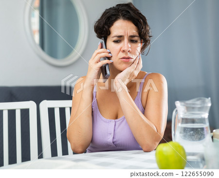 Unhappy woman talking on mobile phone at home 122655090