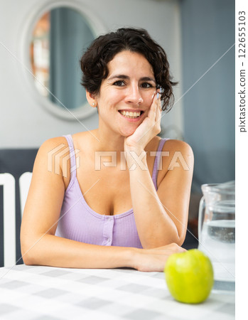 Portrait of smiling young woman sitting at table in home interior 122655103