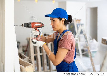 Woman builder using drill to bore hole in wall Woman builder using drill to bore hole in wall 122655114
