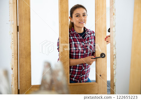 Woman trying on door handles to install on new wooden door 122655223