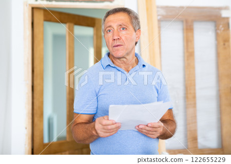 Serious middle-aged casual man exploring a plan of an apartment during renovation 122655229