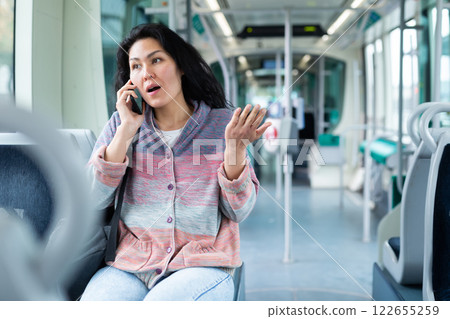 Oriental woman talking on mobile phone while riding a tram 122655259