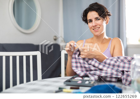 Young woman repairing plaid shirt with needle and thread 122655269