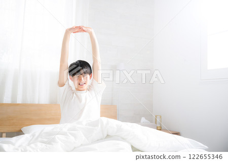 一個年輕人在床上醒來，沐浴著早晨的陽光，伸展著雙臂 122655346