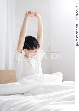 A young man waking up in bed bathed in the morning sun stretching his arms with copy space on the right and eyes closed A young man waking up in bed bathed in the morning sun stretching his arms with copy space on the right and eyes closed 122655348