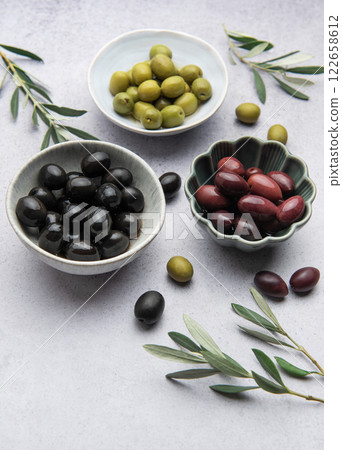 Black, green and kalamata olives with olive branches in bowls on marble 122658612