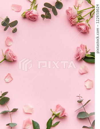 Pink roses and eucalyptus leaves creating a frame on a pink background 122658624