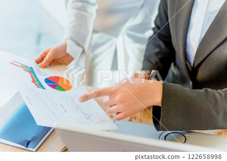 Two women pointing at business documents showing graphs and figures, organizing, analyzing and advising on information 122658998