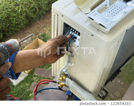 worker connects electric wires to installation of air conditioner 122659283