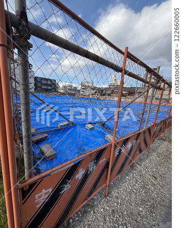 Urban redevelopment site: A vacant lot covered with blue tarpaulin is surrounded by a rusty fence with the words "Safety First" written on it. Urban redevelopment site: A vacant lot covered with blue tarpaulin is surrounded by a rusty fence with the words "Safety First" written on it. 122660005