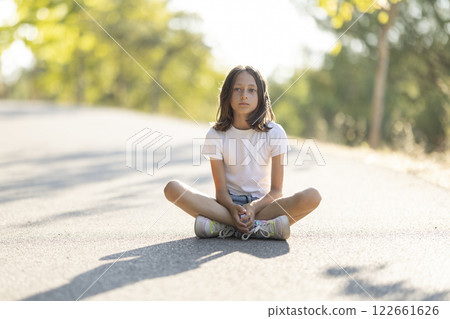 Young girl sitting on sunlit road outdoors Young girl sitting on sunlit road outdoors 122661626