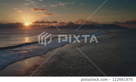 Golden sunset casting a magical glow over a tranquil ocean, with gentle waves lapping at the shore and majestic mountains rising in the background, evokes serenity Golden sunset casting a magical glow over a tranquil ocean, with gentle waves lapping at the shore and majestic mountains rising in the background, evokes serenity 122661970