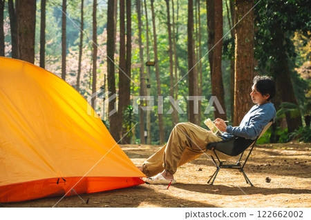 solo traveler in nature concept with asian man camping and work online with pink cherry blossom and pine tree in springtime season 122662002