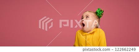 Portrait of adorable child, preschool girl wearing yellow polo shirt, with braided buns hairstyle making shocked face against pink studio background. 122662249